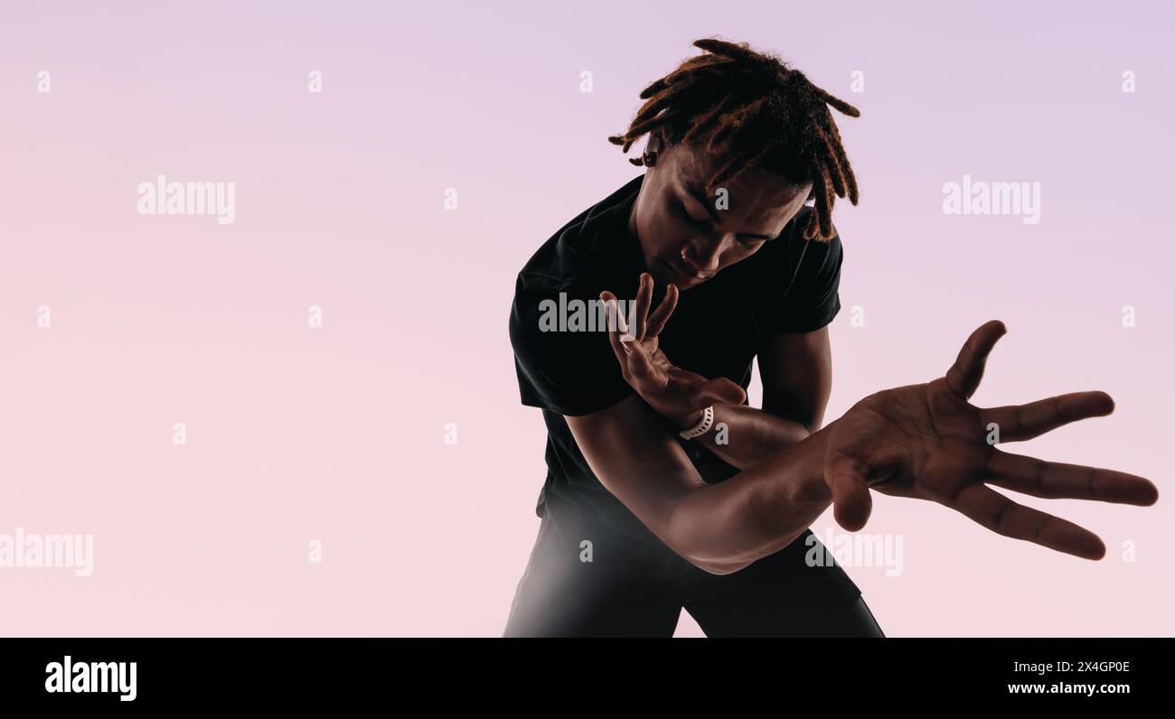 I ritmici uomini della Gen Z ballano energicamente in uno studio, i suoi movimenti espressivi creano una silhouette artistica su uno sfondo rosa. Foto Stock