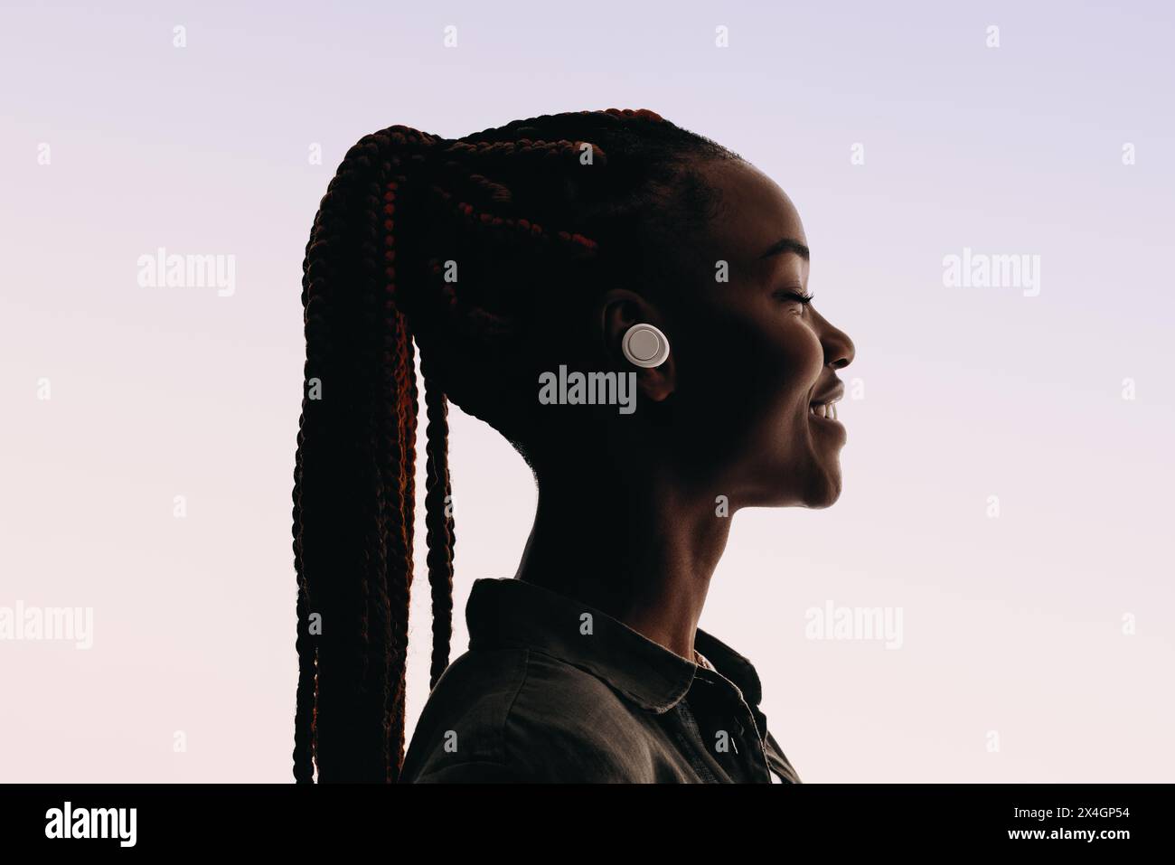La giovane donna africana, felice di 20 anni, con una vista del profilo rilassata, indossa un'elegante coda di cavallo con trecce. Ascolta la musica in modalità wireless. Foto Stock
