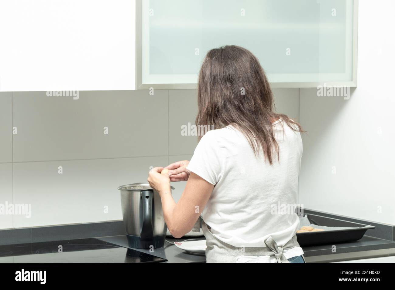 persona che cucina in una cucina moderna, in piedi al piano cottura con una pentola e un vassoio nelle vicinanze Foto Stock