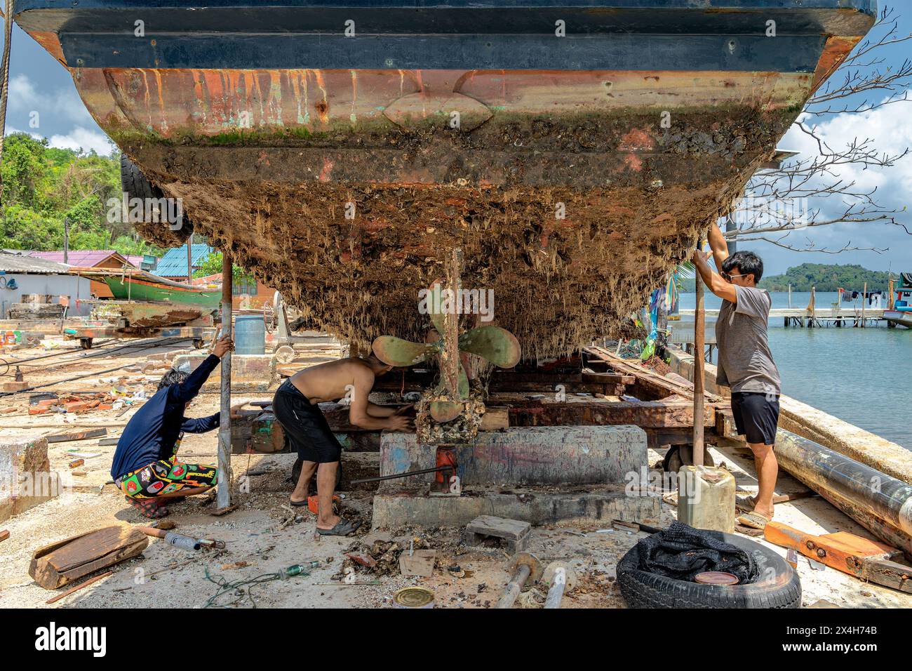 Chanthaburi, Thailandia, 20 marzo 2023: Un addetto alla manutenzione delle imbarcazioni ispeziona la parte inferiore di uno scafo coperto interamente di barnacche e alghe. Foto Stock