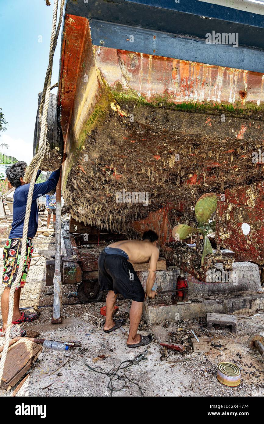 Chanthaburi, Thailandia, 20 marzo 2023: Un addetto alla manutenzione delle imbarcazioni ispeziona la parte inferiore di uno scafo coperto interamente di barnacche e alghe. Foto Stock