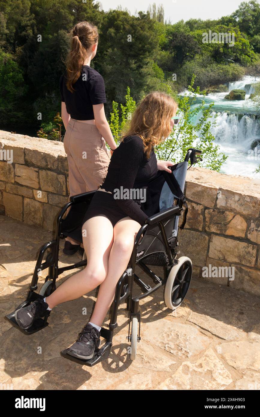 Bambino disabili adolescente turista/ragazza di 14 anni in sedia a rotelle e che si gode il Parco Nazionale di Krka da un punto panoramico, con sua sorella. Croazia. (138) Foto Stock