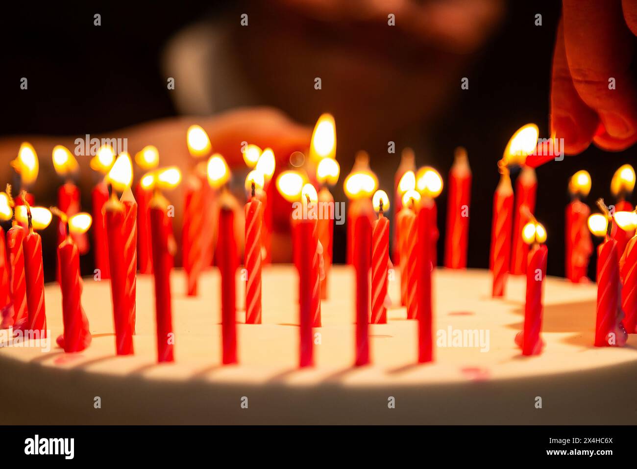 Goiania, Goias, Brasile – 27 aprile 2024: Dettaglio di una mano che accende diverse candele su una torta di compleanno con un volto sfocato sullo sfondo. Foto Stock