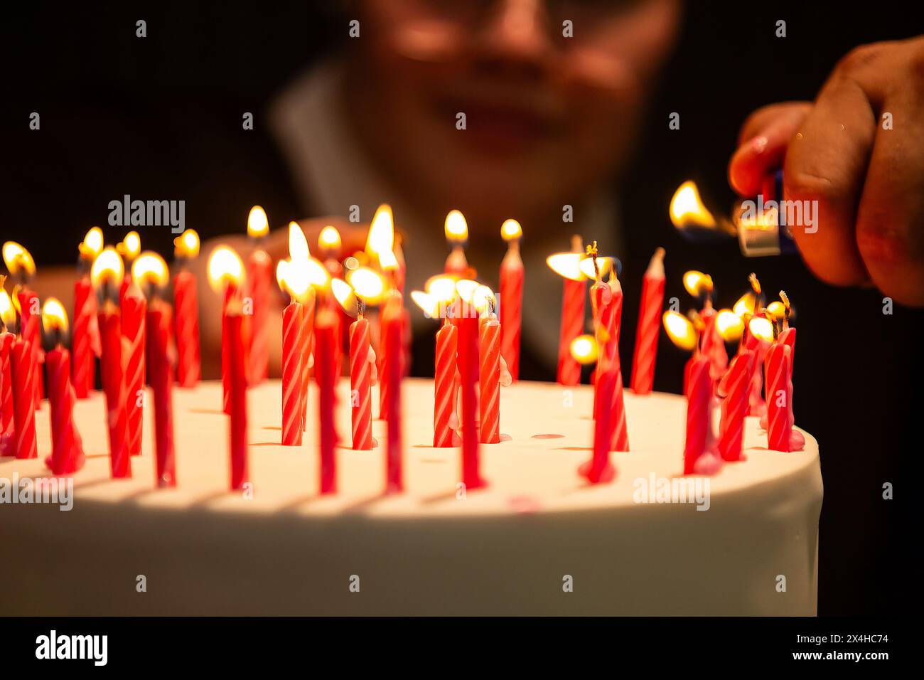 Goiania, Goias, Brasile – 27 aprile 2024: Dettaglio di una mano che accende diverse candele su una torta di compleanno con un volto sfocato sullo sfondo. Foto Stock