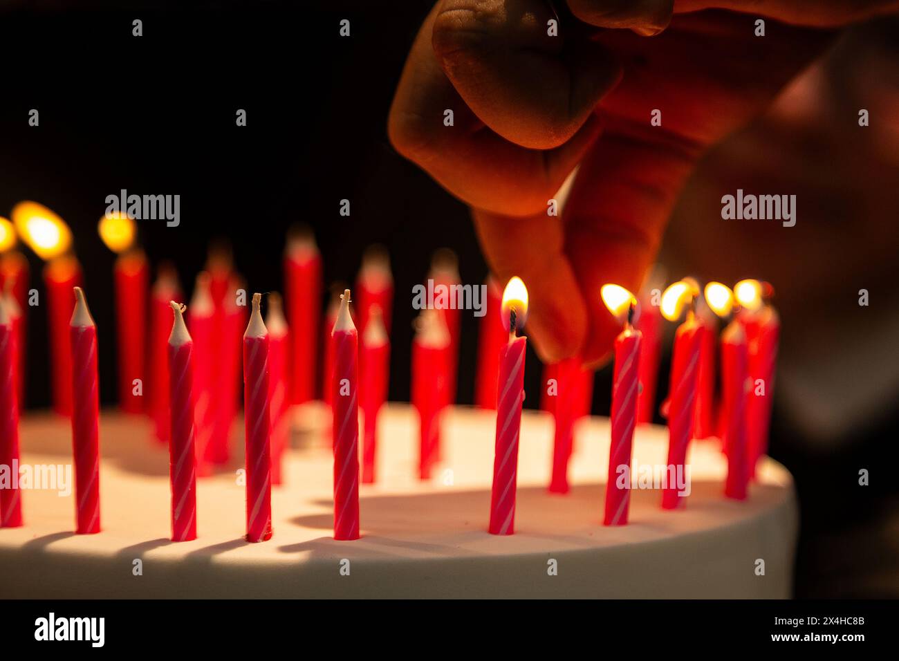 Goiania, Goias, Brasile – 27 aprile 2024: Dettaglio di una mano che mette una candela e diverse altre candele su una torta di compleanno. Foto Stock