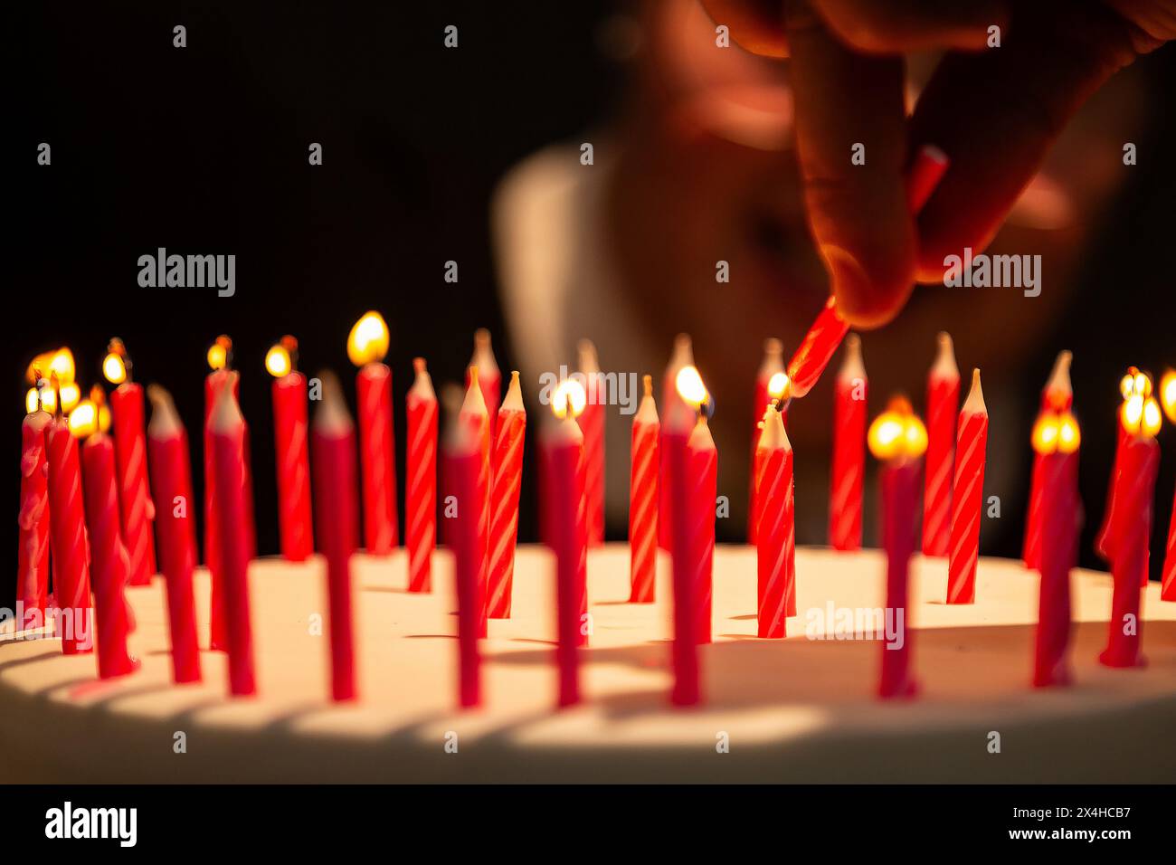 Goiania, Goias, Brasile – 27 aprile 2024: Dettaglio di una mano che accende diverse candele su una torta di compleanno con un volto sfocato sullo sfondo. Foto Stock