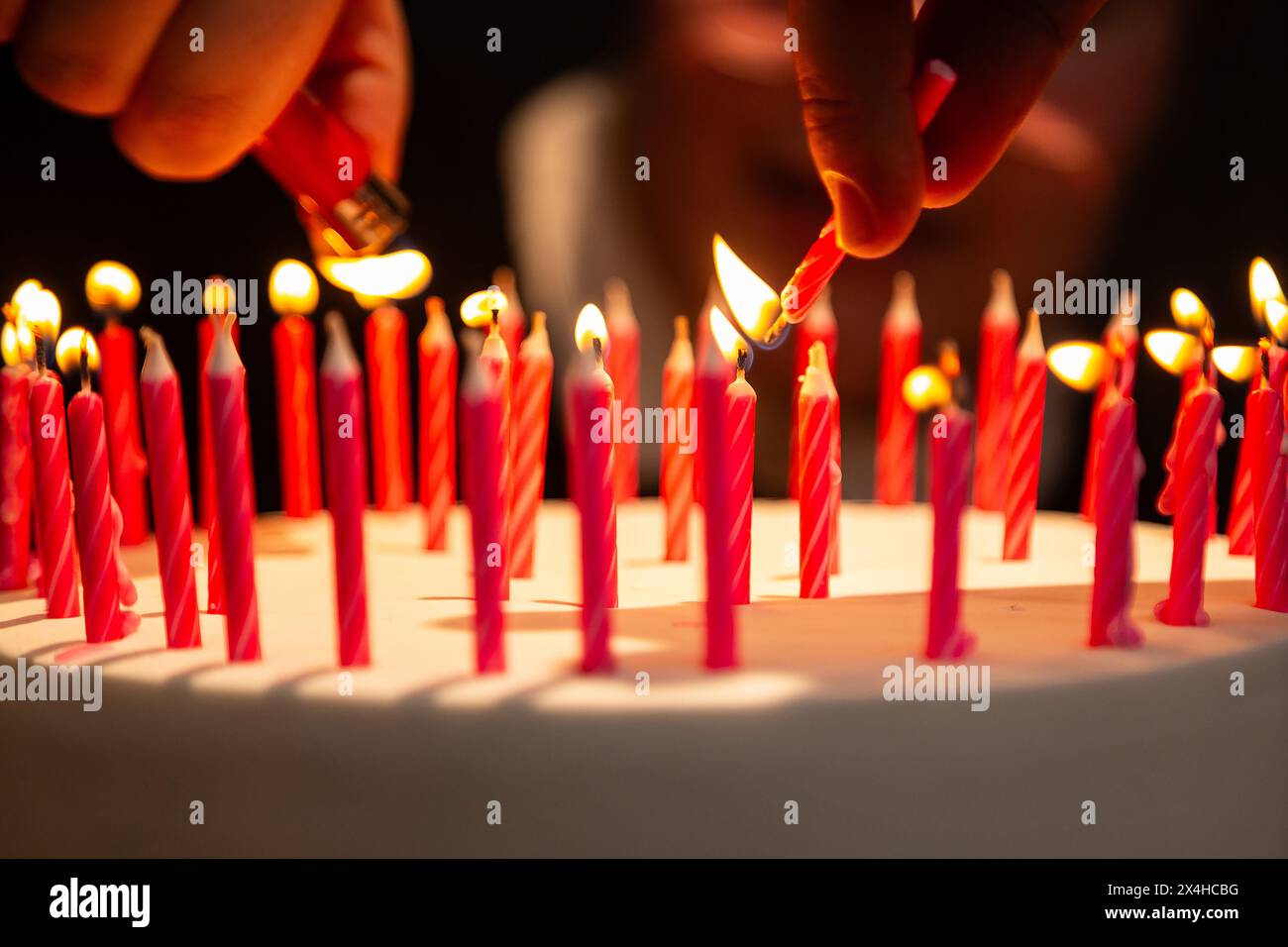 Goiania, Goias, Brasile – 27 aprile 2024: Dettaglio delle mani che illuminano molte candele su una torta di compleanno. Messa a fuoco ristretta. Foto Stock