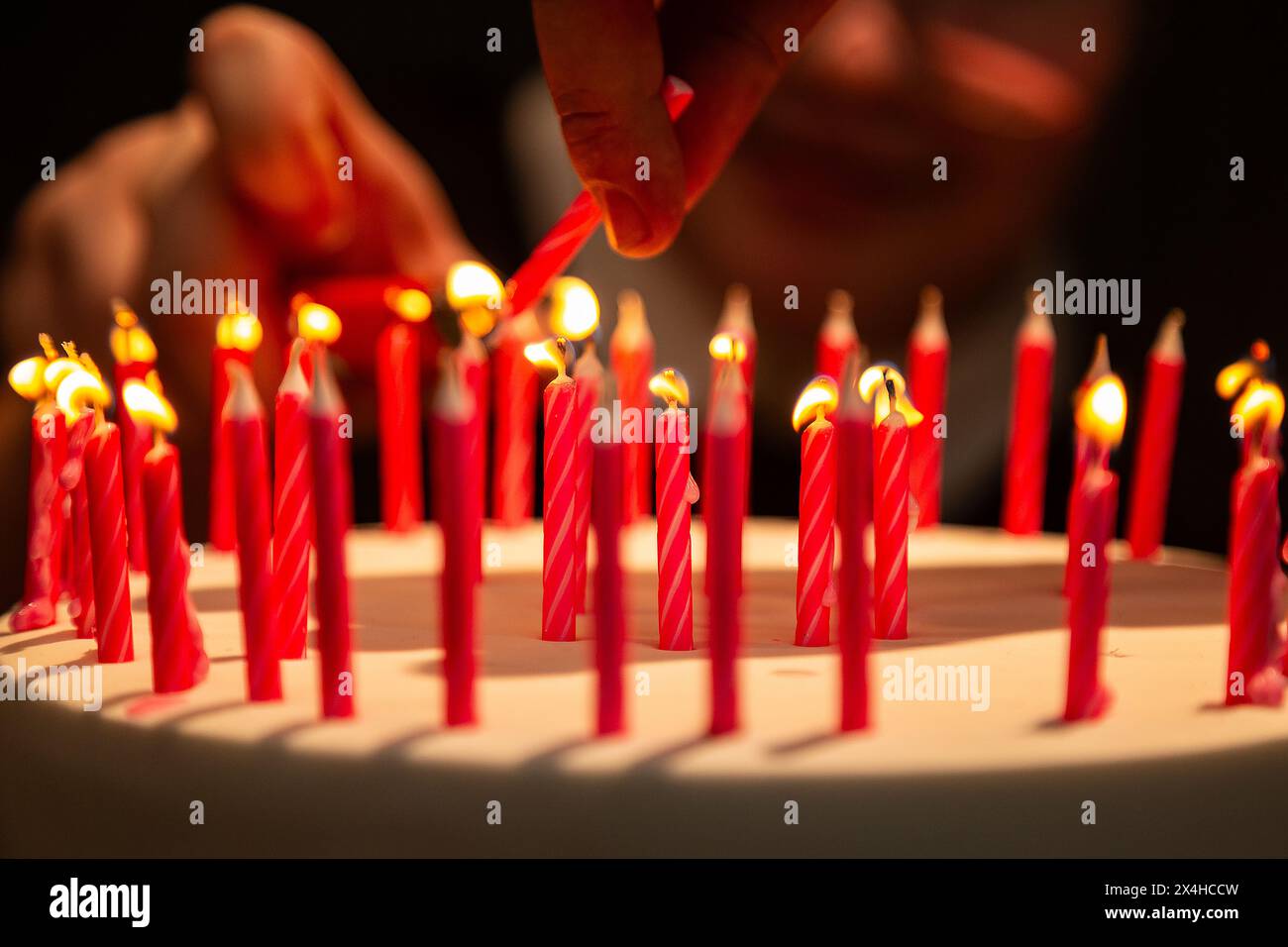 Goiania, Goias, Brasile – 27 aprile 2024: Dettaglio delle mani che illuminano molte candele su una torta di compleanno. Messa a fuoco ristretta. Foto Stock