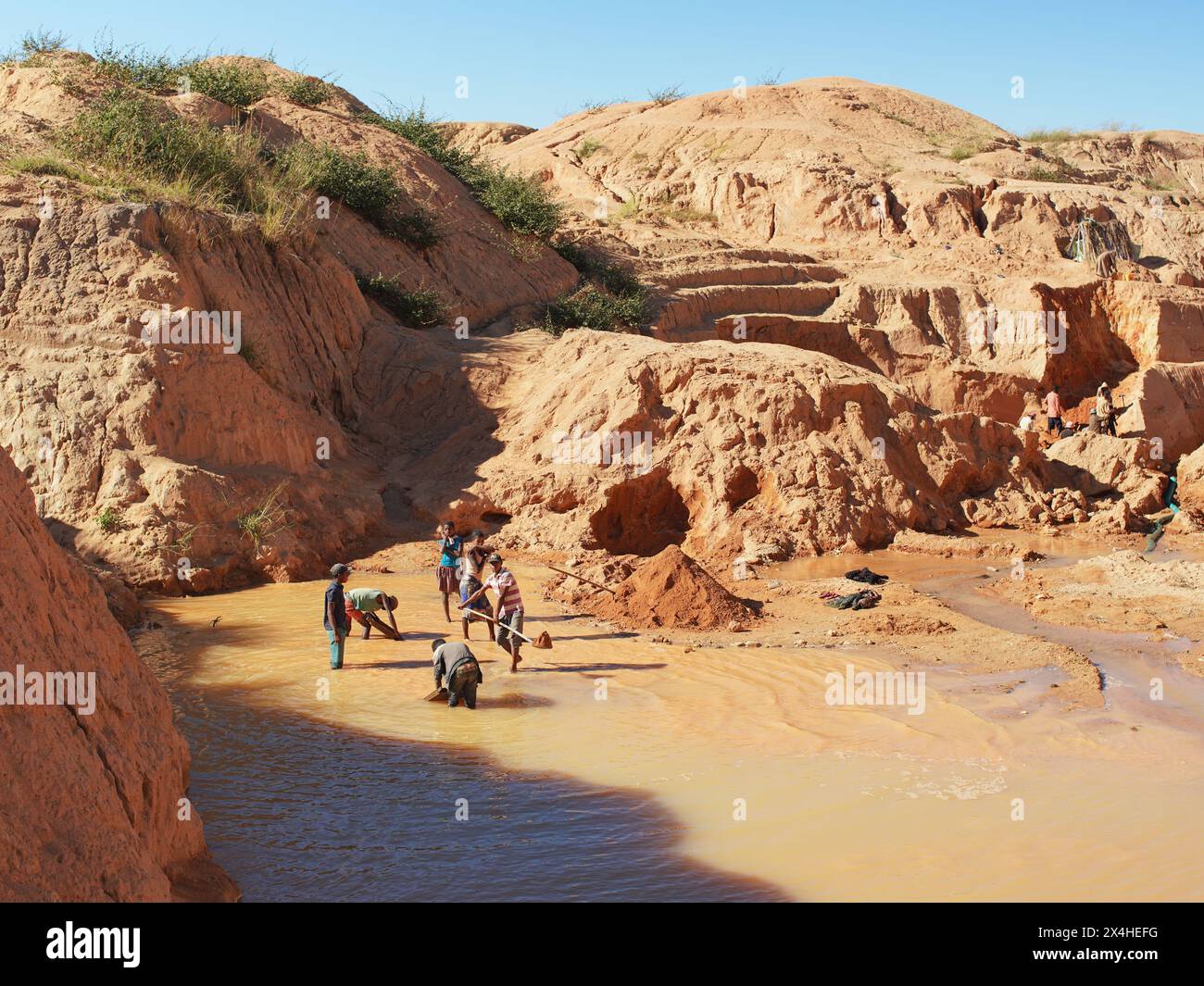 Ilakaka, Madagascar - 30 aprile 2019: Gruppo di malgascio sconosciuti che estraggono zaffiro in miniera di lago di superficie con pale in una giornata di sole, terra rossa secca h Foto Stock