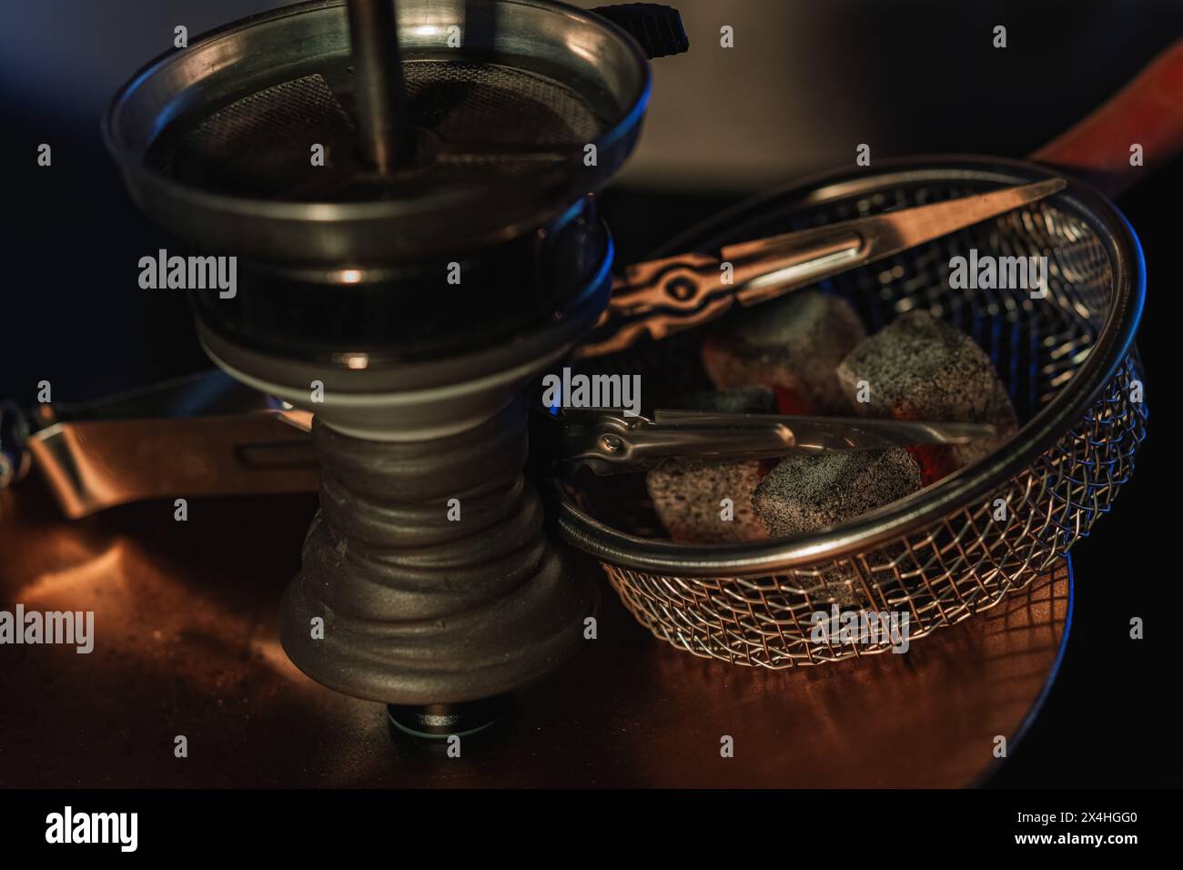 Installazione di narghilè con carboni brillanti in una ciotola in metallo e pinze su una limatura di rame da un narghilè. atmosfera calda e intima di un tradizionale arabo Foto Stock
