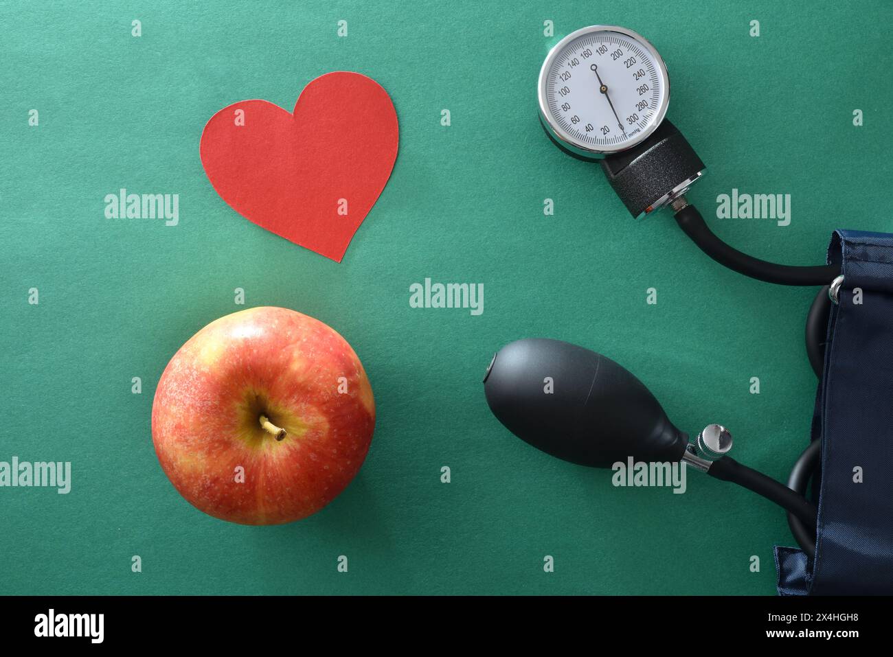 Concetto di controllo della pressione sanguigna con uno stile di vita sano con misuratore della pressione sanguigna mela e ritaglio cardiaco su sfondo verde. Vista dall'alto. Foto Stock