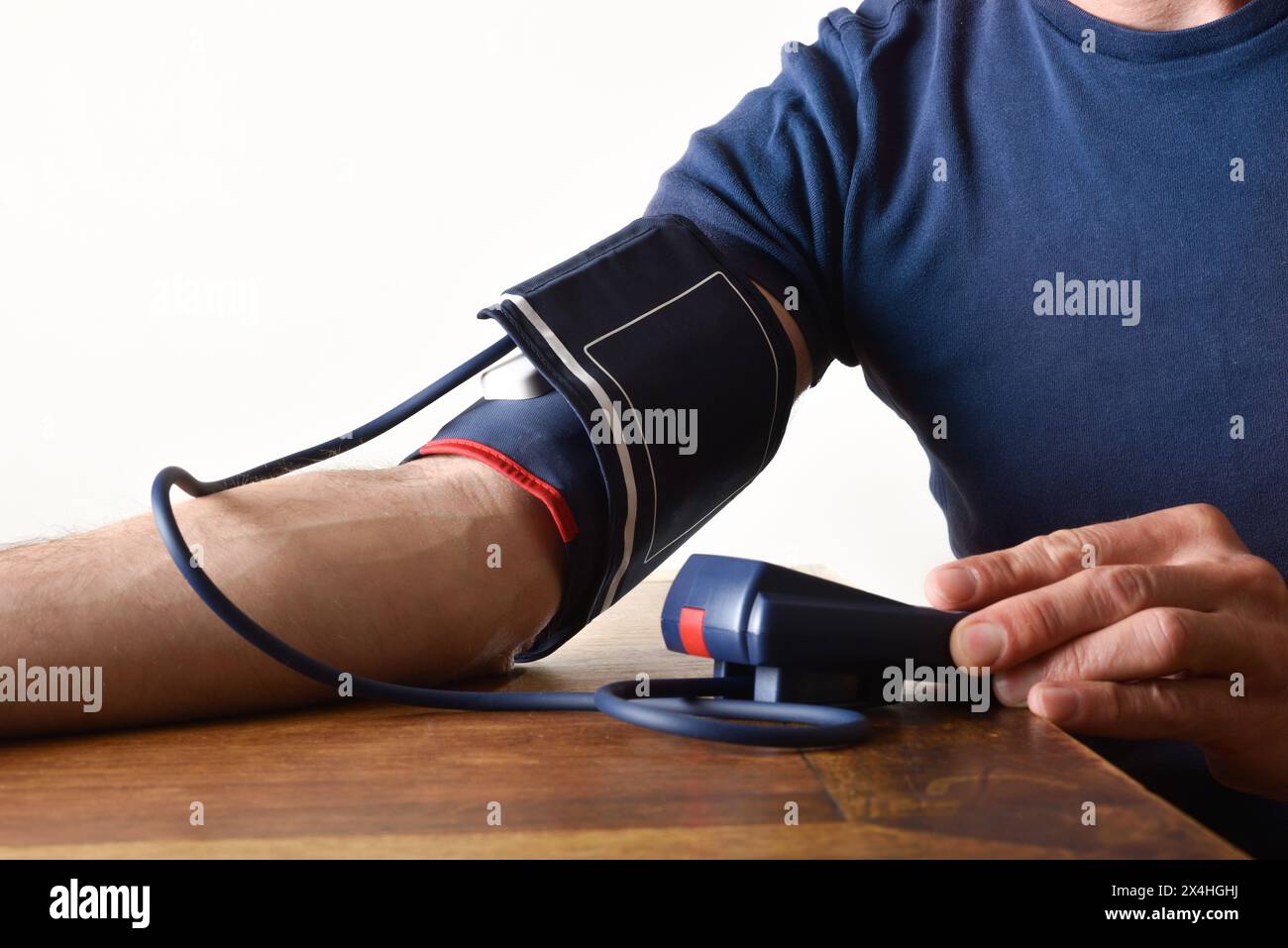 Uomo che prende la pressione sanguigna con un misuratore digitale su un tavolo di legno a casa. Vista laterale. Foto Stock