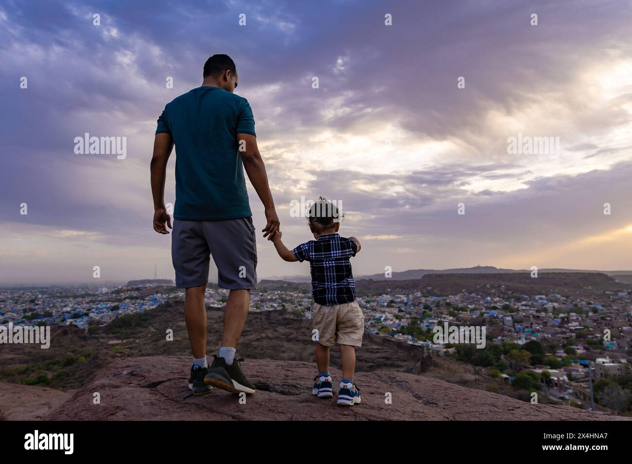 un bambino che tiene la mano al padre ed esplora la natura in cima alla montagna con una vista spettacolare del cielo e della città al crepuscolo, l'immagine viene scattata al mehrangarh jodhpur rajasthan Foto Stock