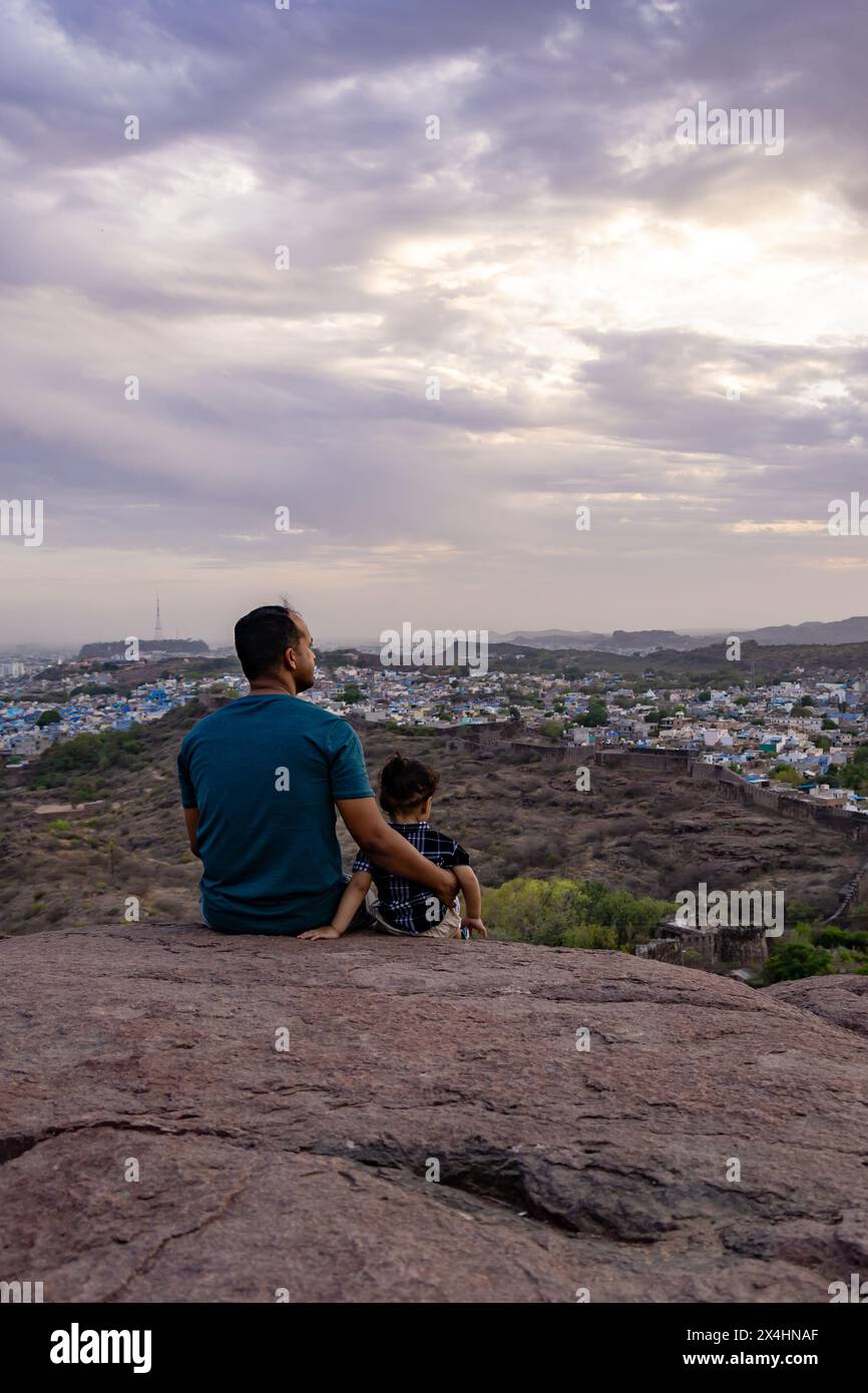 isolare padre e figlio neonato osservando il paesaggio della città in cima alla montagna con un cielo spettacolare al tramonto Foto Stock