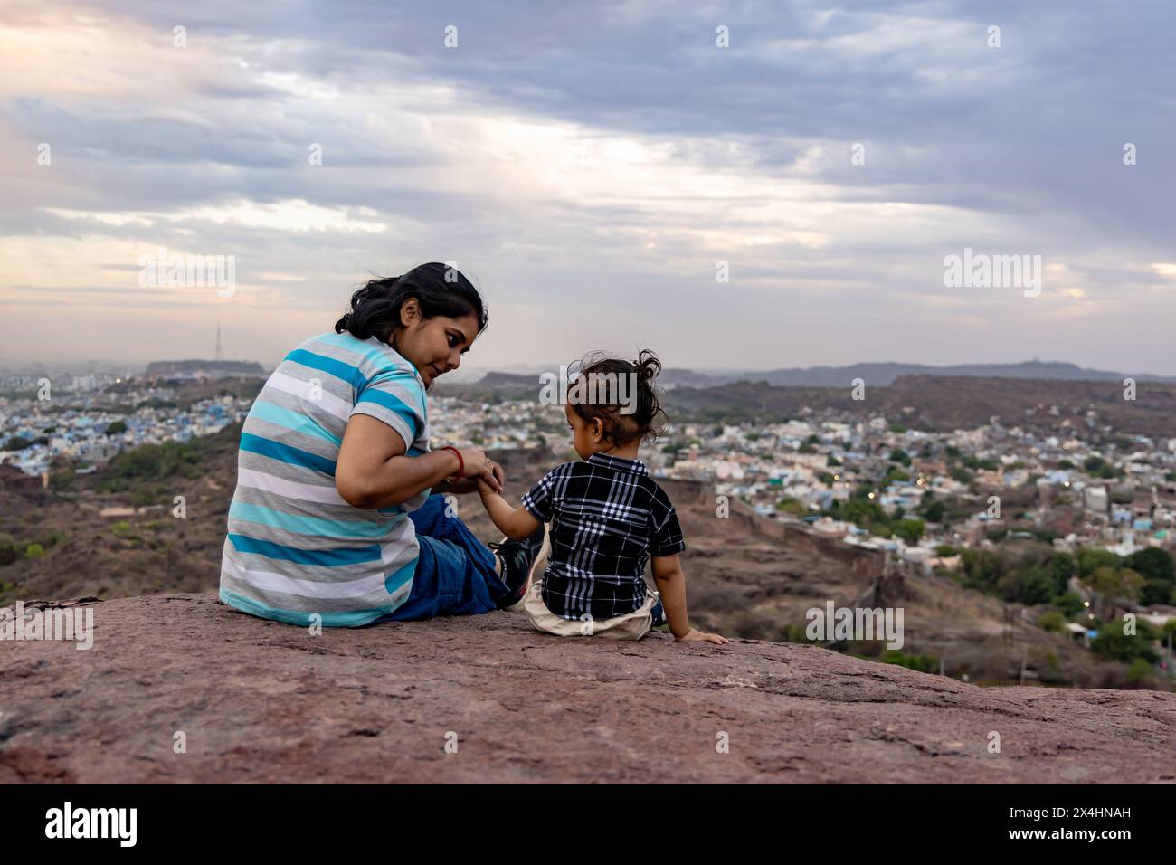 isola madre e figlio neonato guardando il paesaggio della città in cima alla montagna con un cielo spettacolare al crepuscolo immagine è scattata a mehrangarh jodhpur rajasthan india. Foto Stock