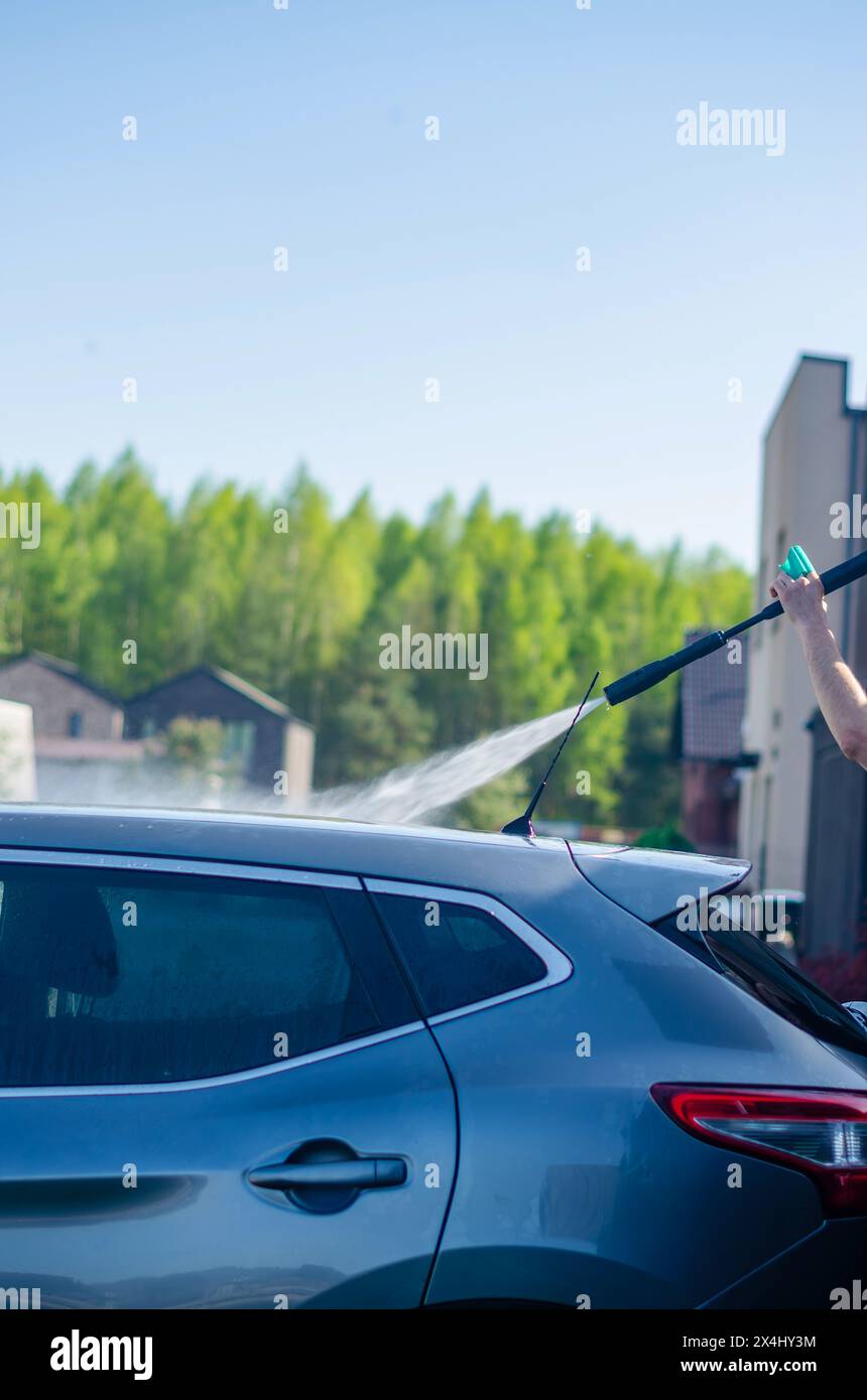 Un uomo lava un'auto nera con una pompa ad alta pressione. Con l'aiuto di una lavatrice portatile. Foto di alta qualità Foto Stock