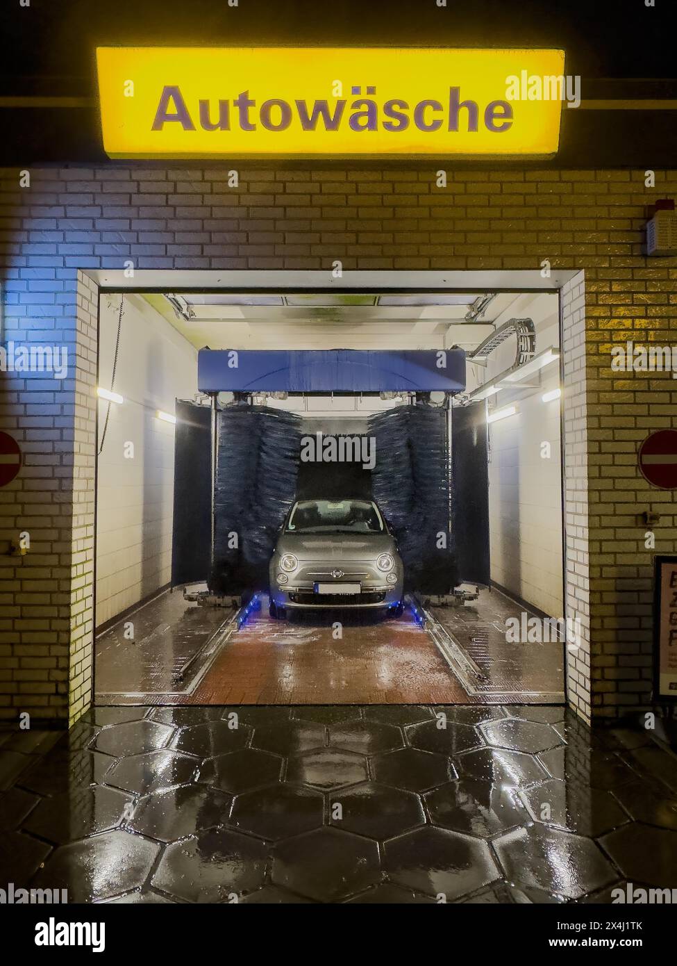 Vista della Fiat 500 in autolavaggio di notte con spazzole rotanti spazzole tessili per autolavaggio automatico sopra cartello illuminato con scritta auto Foto Stock