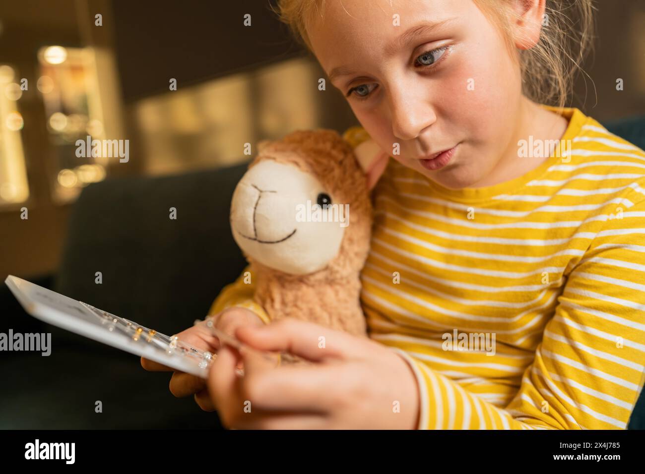 Ragazza sorridente che tiene in mano un giocattolo imbottito e mostra orecchini, guardando un orecchino in una gioielleria Foto Stock