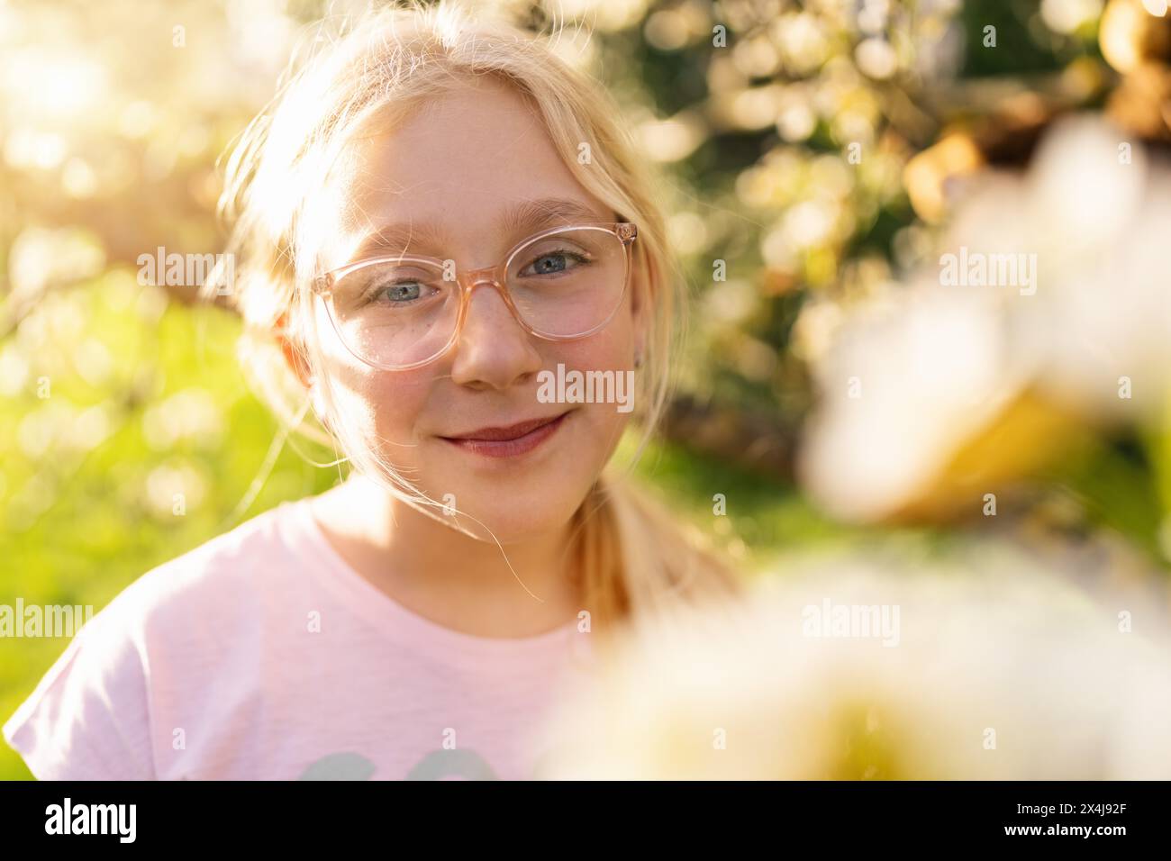 Primo piano di una ragazza con gli occhiali sorridenti in piedi in un albero di mele in fiore in primavera Foto Stock