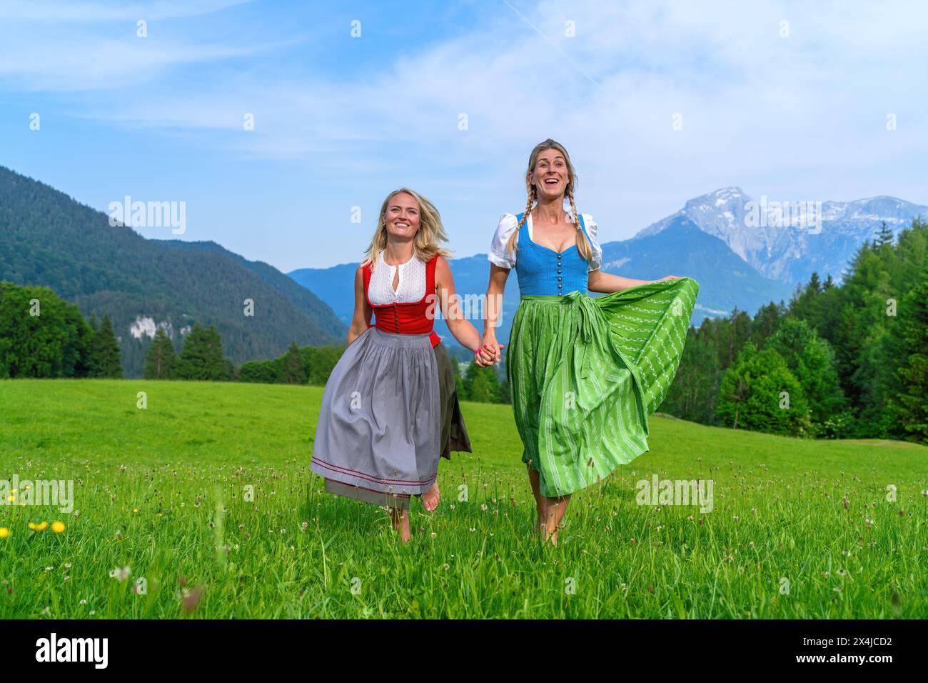 Amici felici in abiti bavaresi tradizionali, Dirndl o tracht che si tengono per mano e si attorcigliano in un prato estivo sulle montagne dell'alpe tedesca Foto Stock