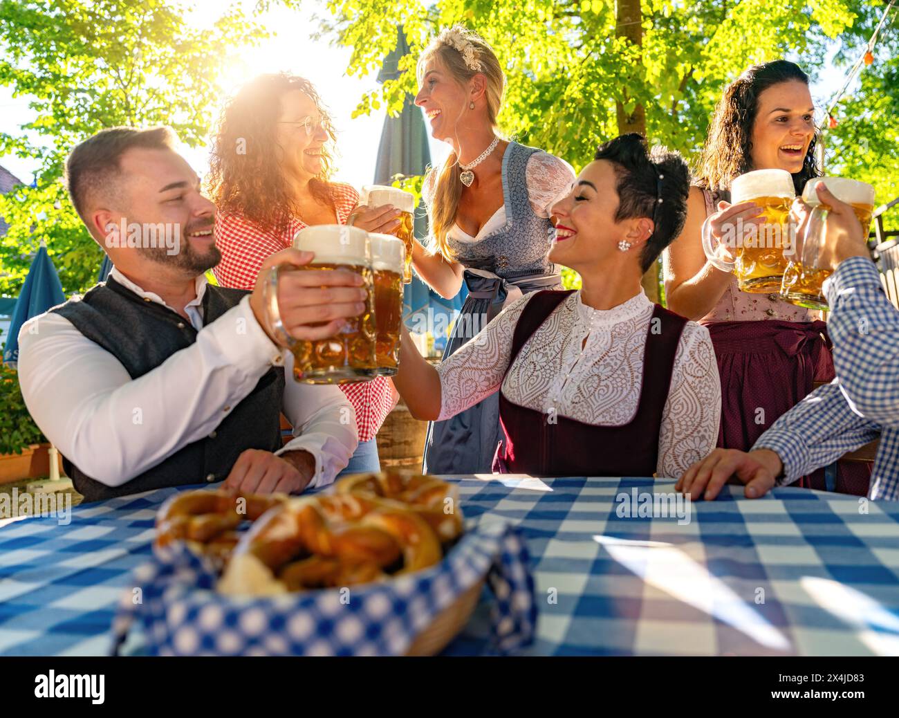 Amici seduti nella birreria all'aperto o nell'oktoberfest con bicchieri di birra che si brindano a vicenda in Baviera, Germania Foto Stock