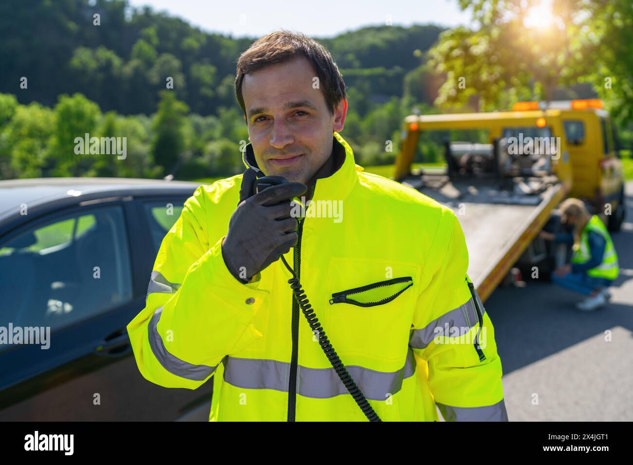 Operatore di un autocarro che parla su un walkie-talkie che guarda la telecamera per caricare un'auto danneggiata su un autocarro. Foto Stock