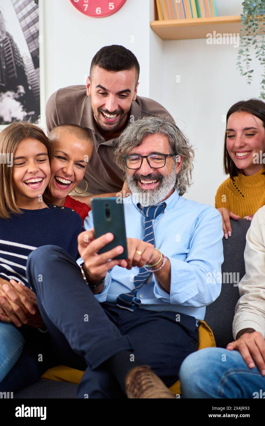 Famiglia caucasica multigenerazionale si riunì nel soggiorno seduto sul divano utilizzando il telefono cellulare. Foto Stock