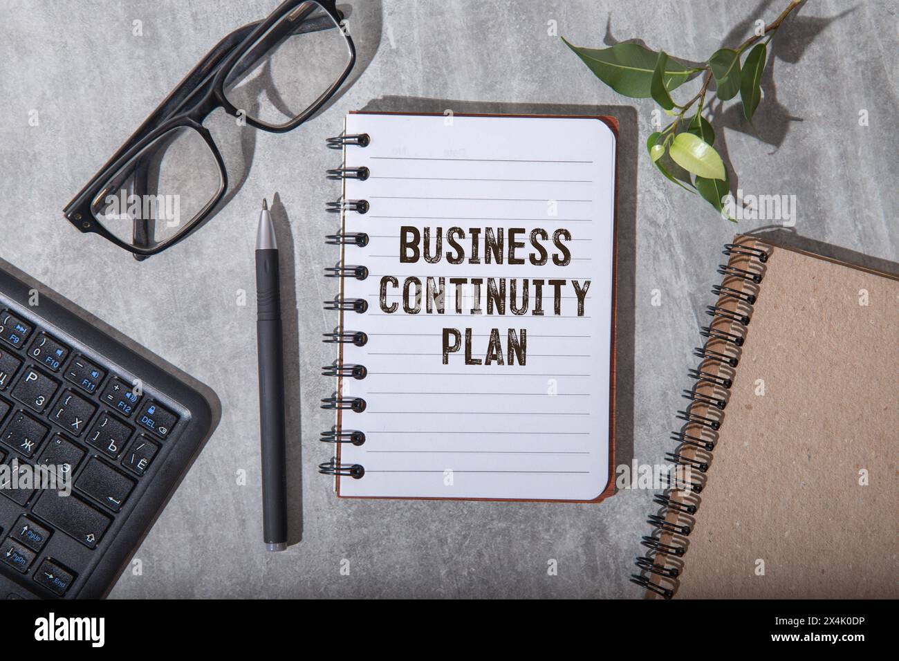 Su uno sfondo grigio chiaro si trovano una penna, un notebook verde e un biglietto bianco con il testo BCP Business Continuity Plan. Concetto aziendale. Foto Stock