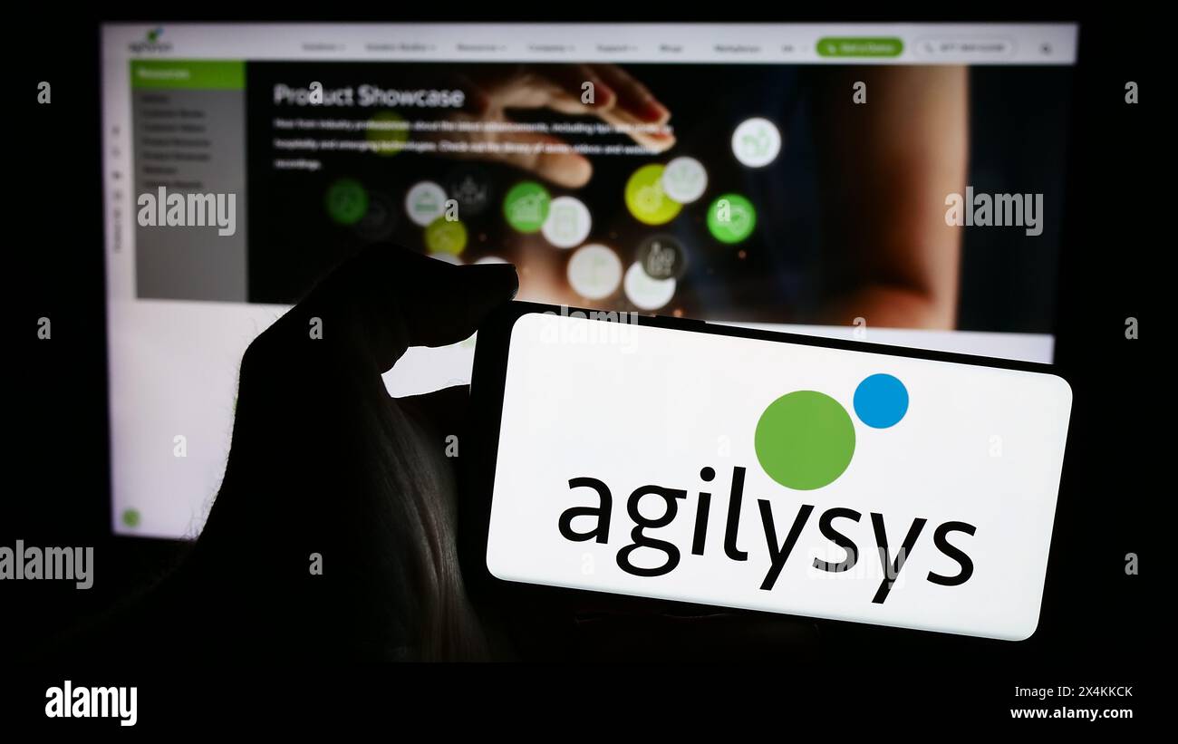 Persona che possiede uno smartphone con il logo della società di software aziendale statunitense Agilysys Inc. Davanti al sito Web. Mettere a fuoco il display del telefono. Foto Stock