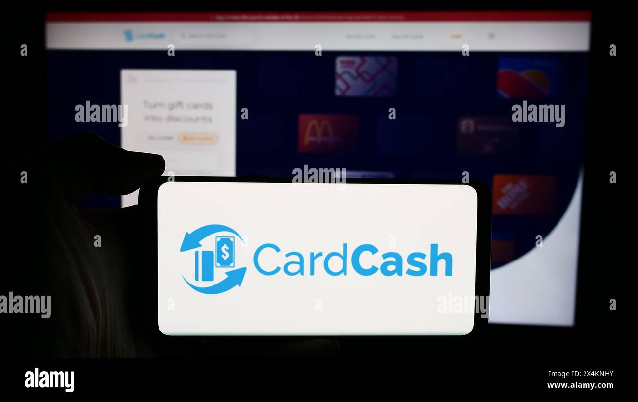Persona che detiene un cellulare con il logo della società statunitense CardCash che si occupa del mercato delle carte regalo davanti alla pagina Web aziendale. Mettere a fuoco il display del telefono. Foto Stock