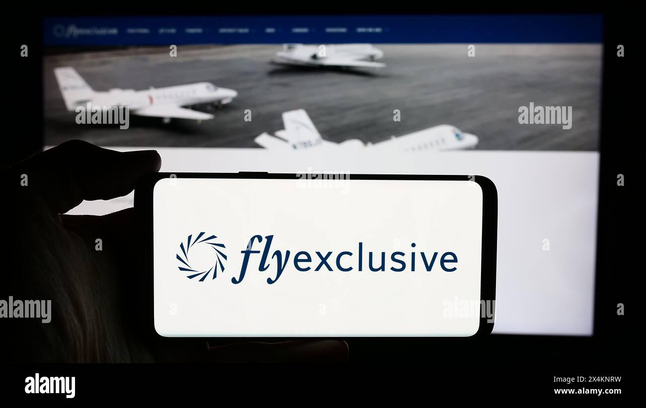 Persona che detiene un cellulare con il logo della società jet privata statunitense flyExclusive Inc. Di fronte alla pagina Web aziendale. Mettere a fuoco il display del telefono. Foto Stock
