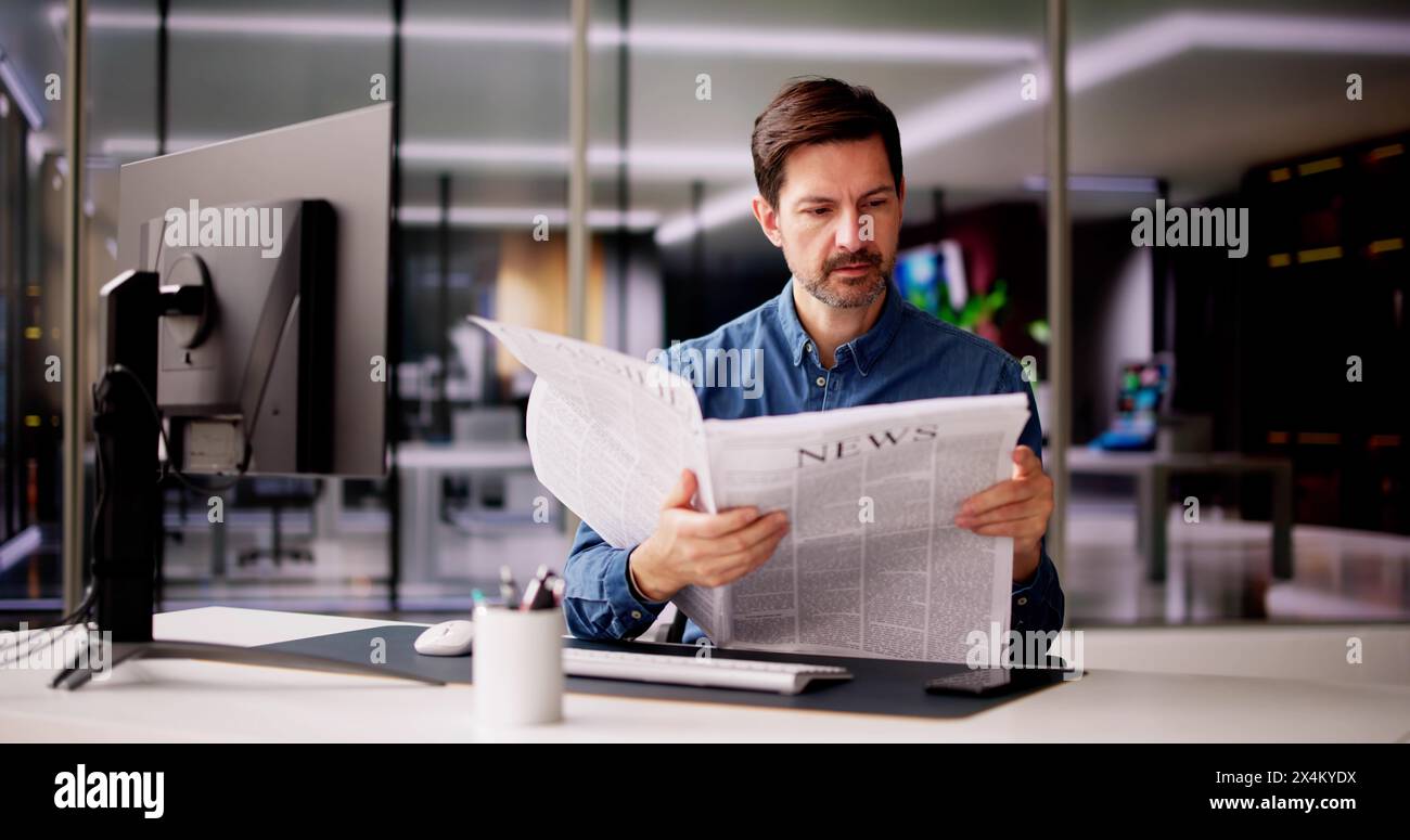 Uomo d'affari che legge il giornale alla scrivania al lavoro Foto Stock