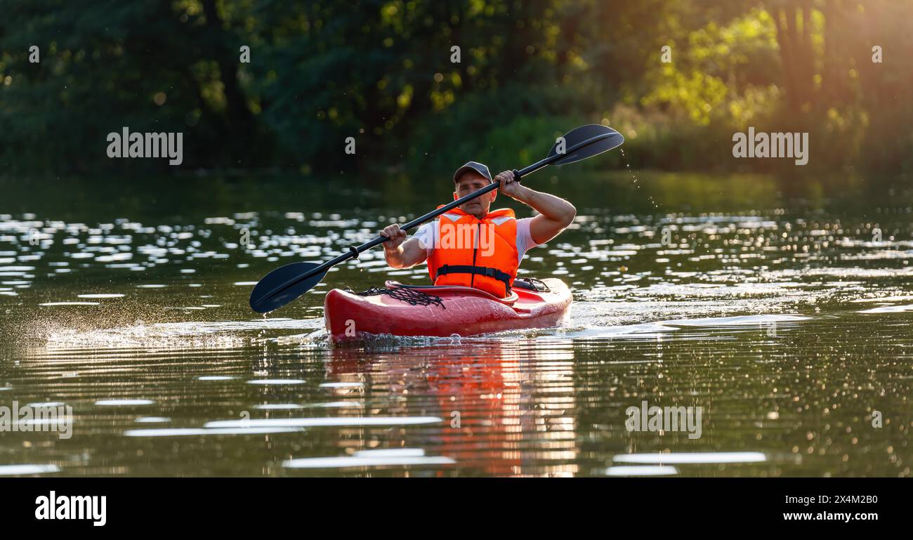 Uomo concentrato su un kayak rosso su un fiume scintillante, pagaiando con la concentrazione alla luce della sera in germania. Immagine del concetto di kayak Water Sports Foto Stock