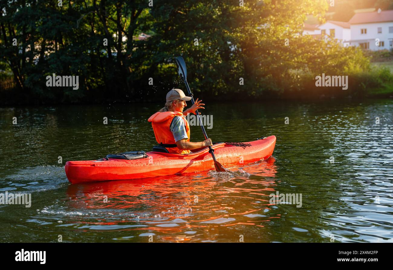 donna in kayak gioiosamente su un fiume sereno al tramonto, circondato da una vegetazione lussureggiante in estate in germania. Immagine del concetto di kayak Water Sports Foto Stock