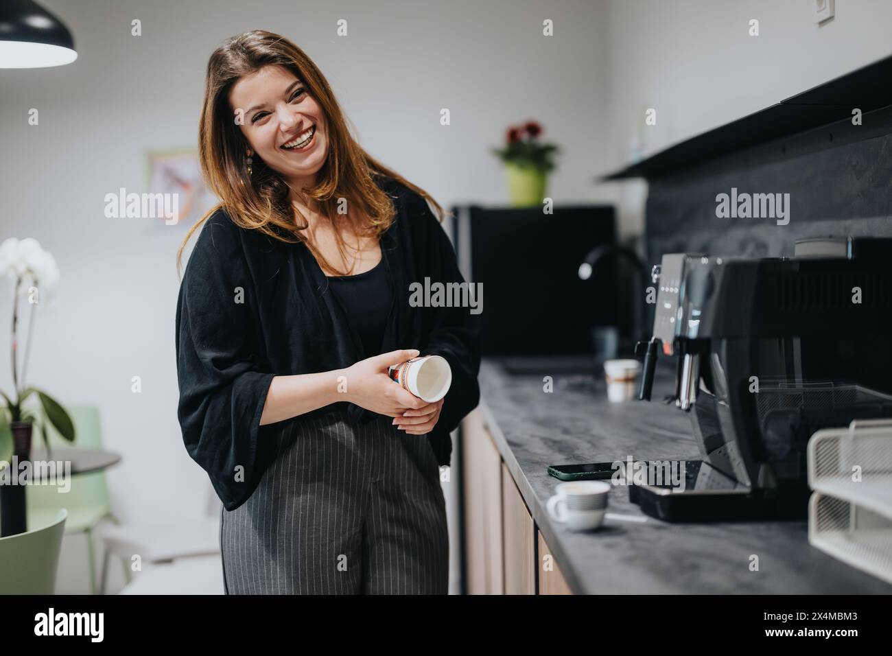 Giovane donna d'affari che si gode una pausa caffè in una moderna cucina dell'ufficio Foto Stock