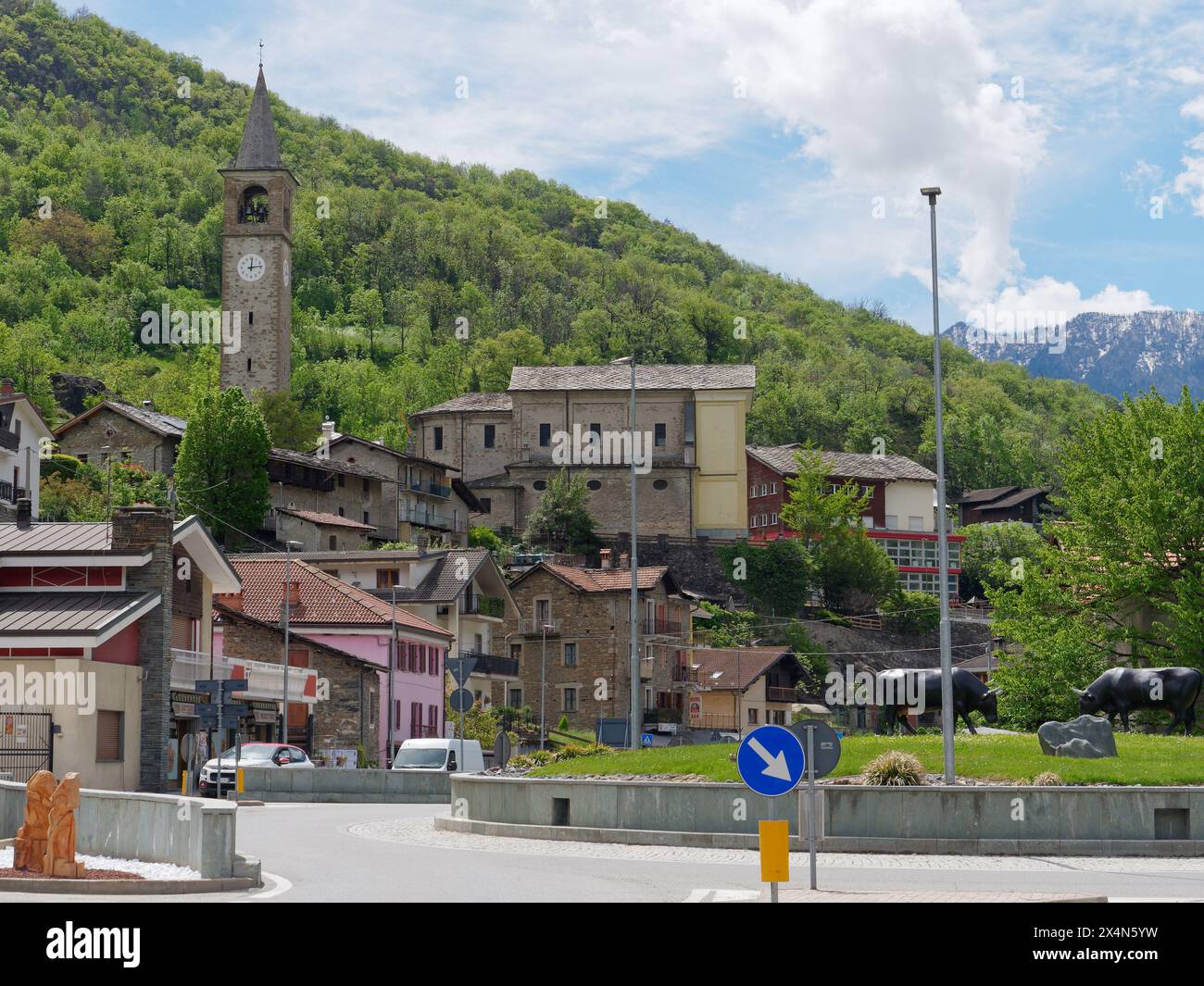 La città di Montjovet con la sua torre dell'orologio e le statue del toro su una rotatoria nella Valle d'Aosta, NW Italia. 4 maggio 2024 Foto Stock