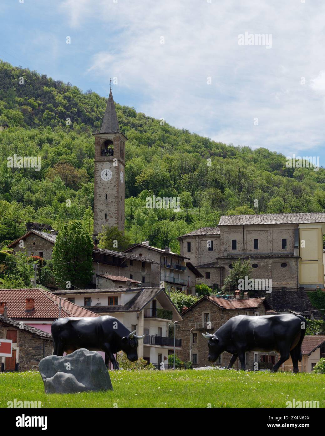 La città di Montjovet con la sua torre dell'orologio e le statue del toro su una rotatoria nella Valle d'Aosta, NW Italia. 4 maggio 2024 Foto Stock