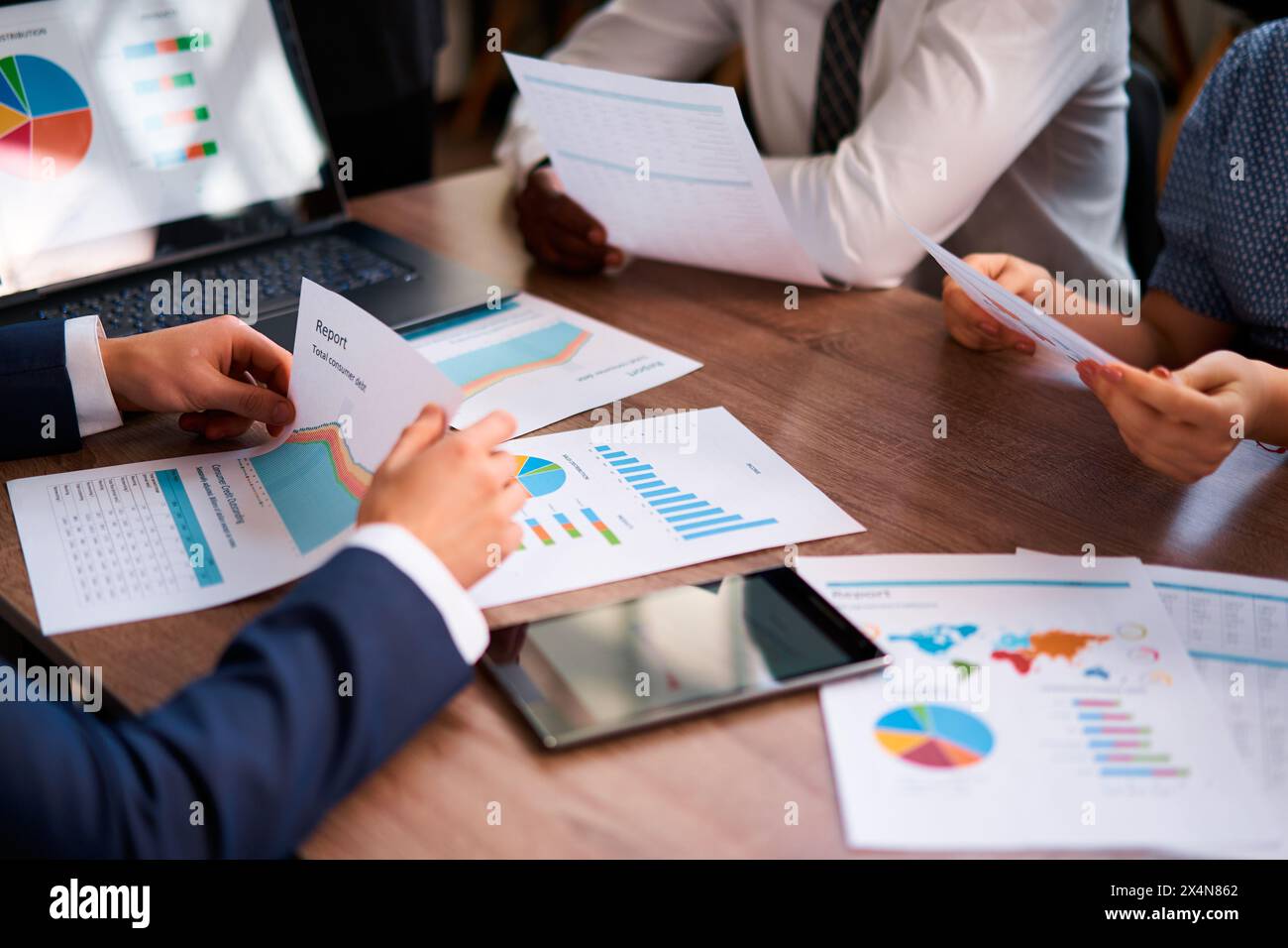 Il team multietnico analizza le metriche aziendali sul luogo di lavoro, discutendo grafici colorati sui report e sulla strategia di pianificazione. Il gruppo aziendale collabora Foto Stock