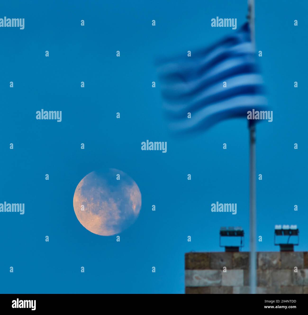 Luna piena al buio accanto a una bandiera sfocata al crepuscolo, al porto di Mandraki, Rodi, Dodecaneso, isole greche, Grecia Foto Stock