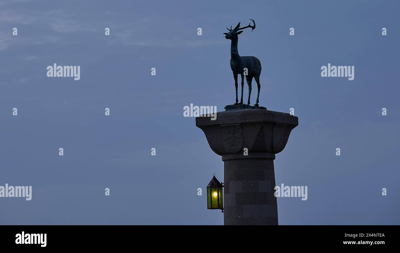 Statua di cervo su colonna con lanterna illuminata al crepuscolo, Mandraki OAT, Rodi, Dodecaneso, isole greche, Grecia Foto Stock