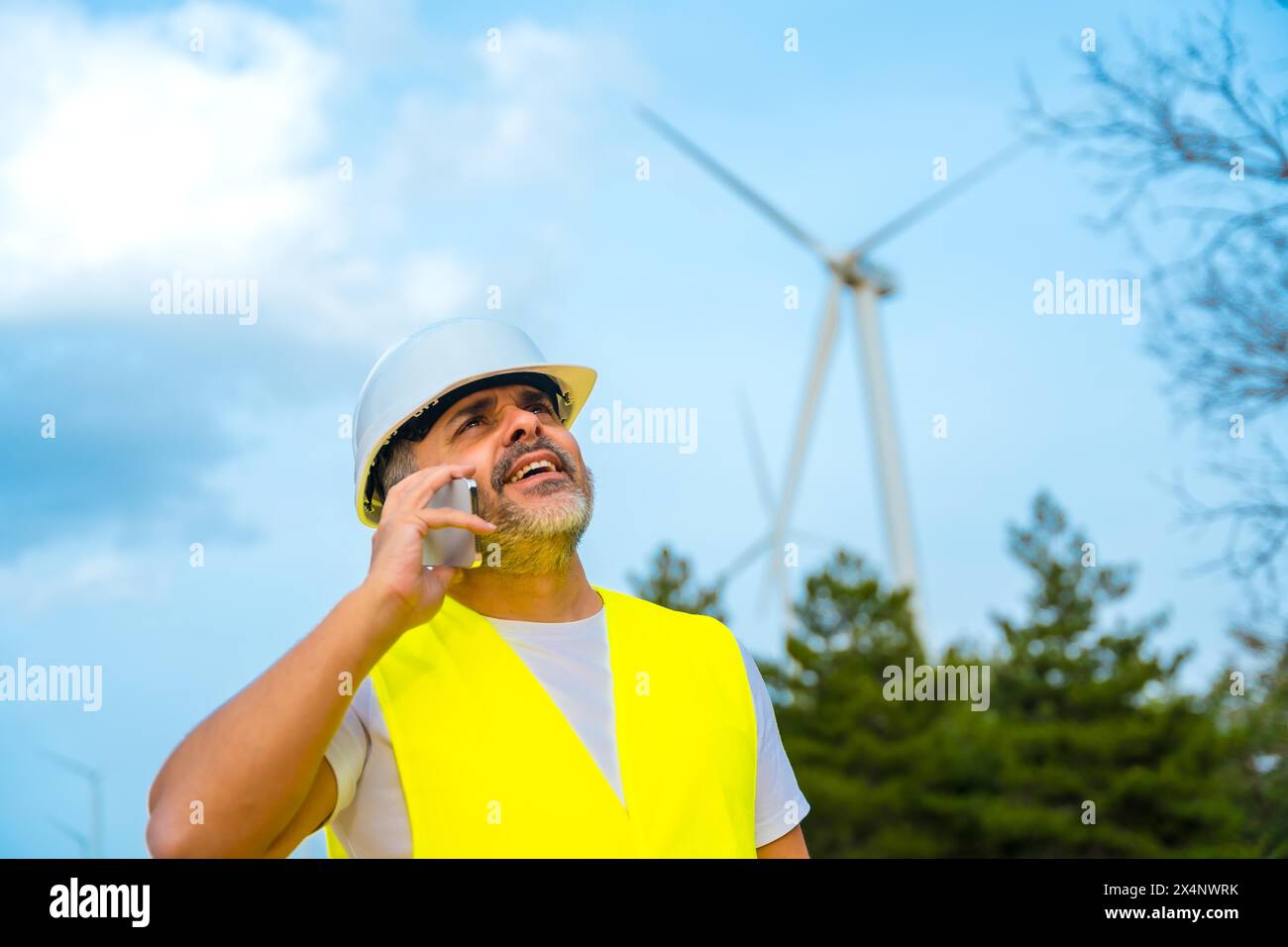 Lavoratore che indossa l'attrezzatura di sicurezza che parla con il telefono cellulare in un parco eolico Foto Stock