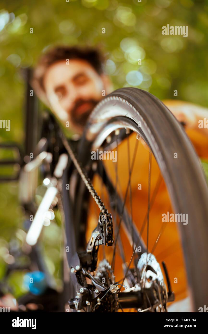 Colpo dettagliato di catena di gomma ruota bicicletta in corso di esame e manutenzione da giovane uomo caucasico sano all'aperto. Immagine che mostra una vista ravvicinata delle ruote della ruota e delle pulegge in cortile. Foto Stock