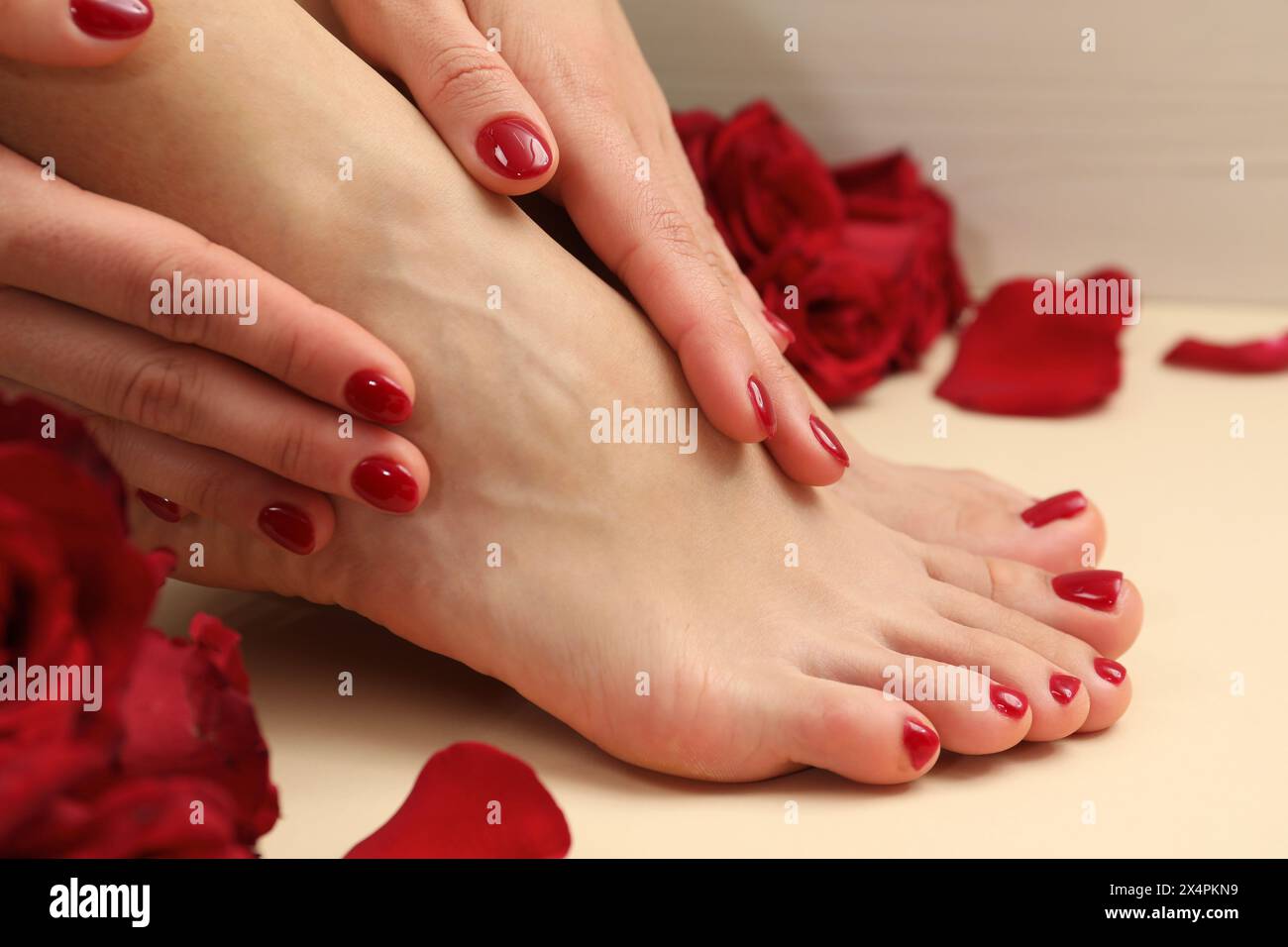 Donna con eleganti unghie rosse dopo la procedura di pedicure e petali di rosa su sfondo beige, primo piano Foto Stock