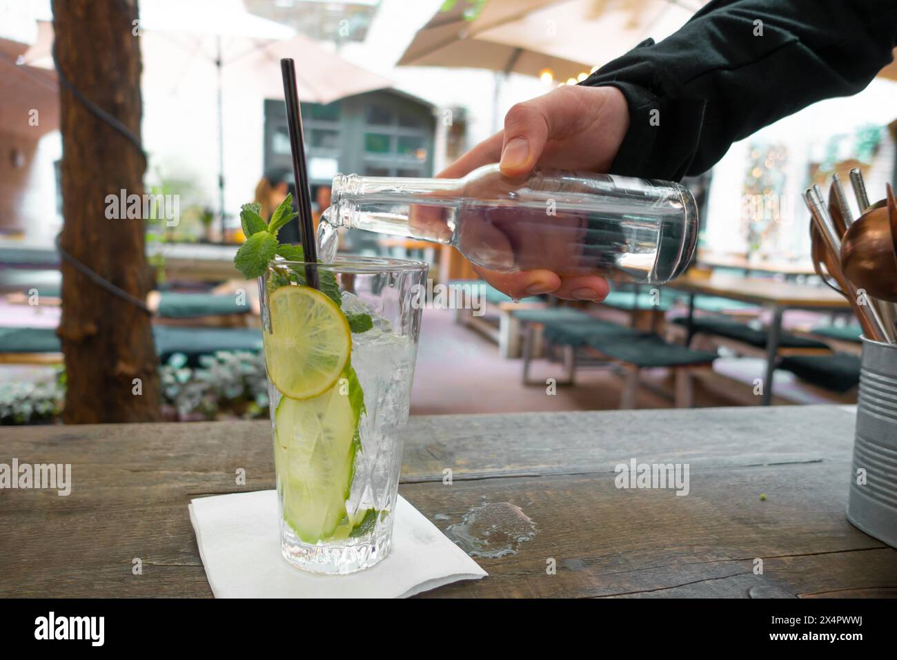 Limonata con limone fresco su sfondo tavolo di legno. la mano di un uomo in una manica nera versa una bevanda gassata in un alto vetro trasparente, in cui Foto Stock