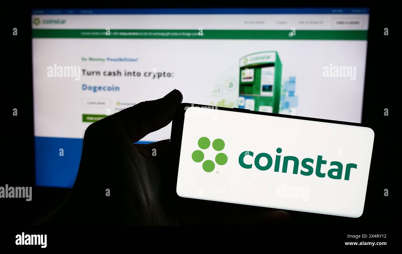 Persona che detiene uno smartphone con il logo della società statunitense Coinstar LLC di fronte al sito web. Mettere a fuoco il display del telefono. Foto Stock