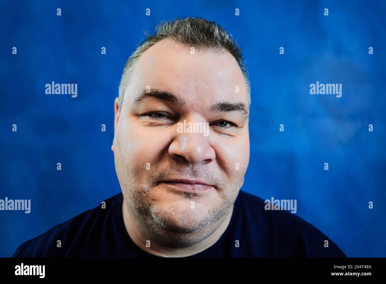 Sly volto dell'uomo caucasico, primo piano di 47 anni su sfondo blu. Foto Stock