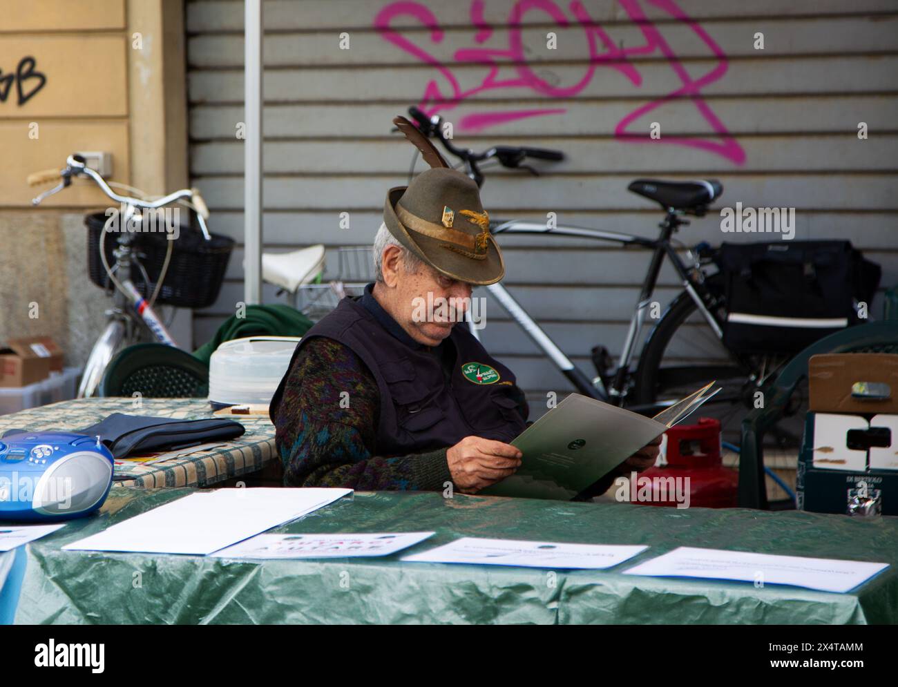 Uomo che indossa un cappello militare alpino italiano seduto dietro il bancone al festival del villaggio Foto Stock