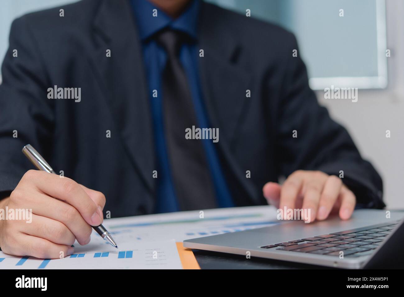 Un professionista esamina i rapporti analitici su un laptop, una penna in mano. La scena cattura l'essenza della pianificazione strategica e della performance Foto Stock