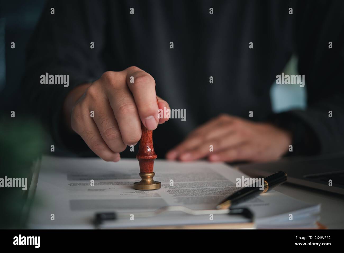 Persona concentrata che posiziona un sigillo su un documento ufficiale con francobollo di cera rosso in un ambiente professionale Foto Stock