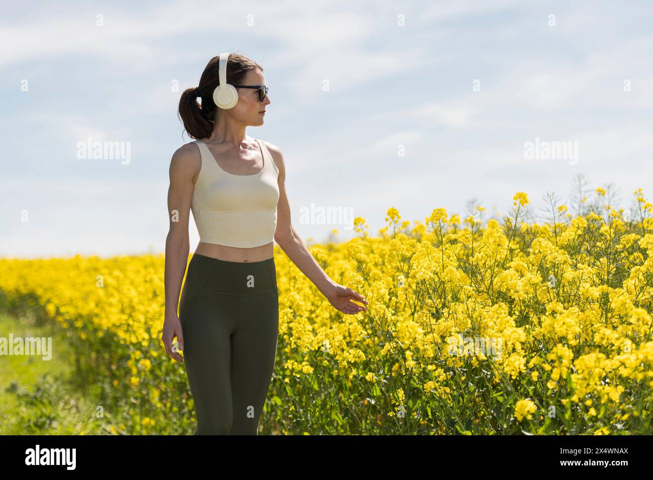 Donna che indossa le cuffie che cammina in campagna, sfondo giallo del campo Foto Stock